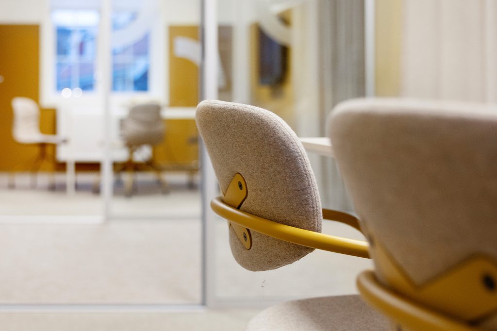 Konseptuelt interiørdesign. Møteromsstoler med sete- og ryggtrekk i beige og ben og armlener i okergult metall.